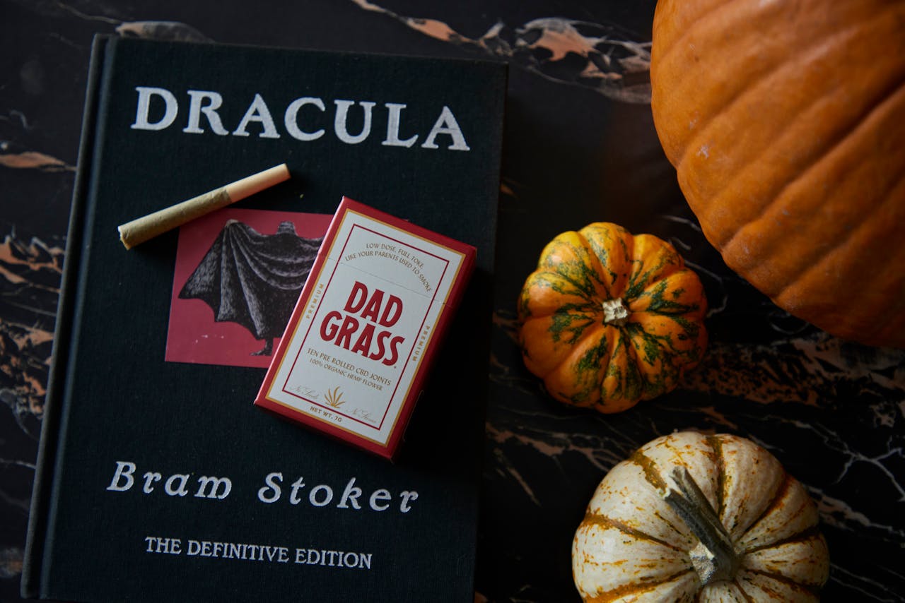 Embrace Halloween with Dracula, mini pumpkins, and CBD pre-rolls in a cozy flat lay.