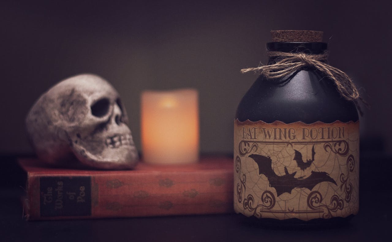 Spooky still life with skull, bat potion bottle, candle, and book.